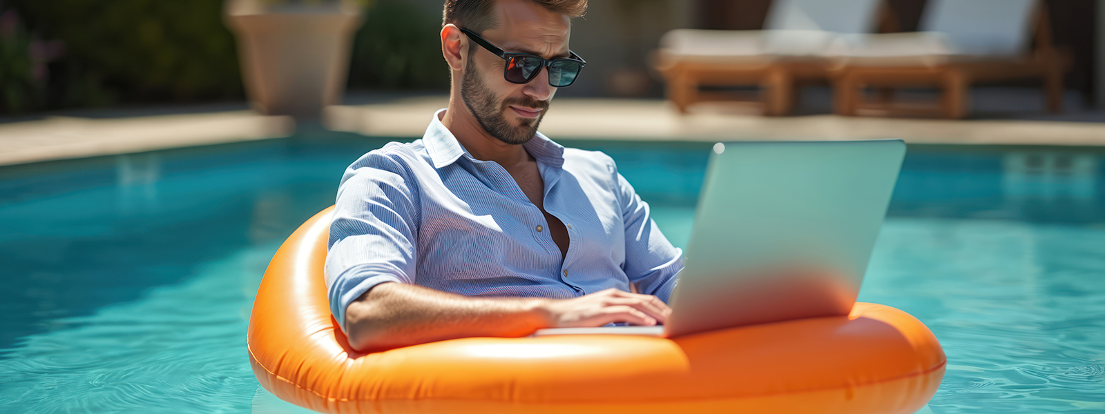 A young executive on a laptop while floating on an inner tube in a pool