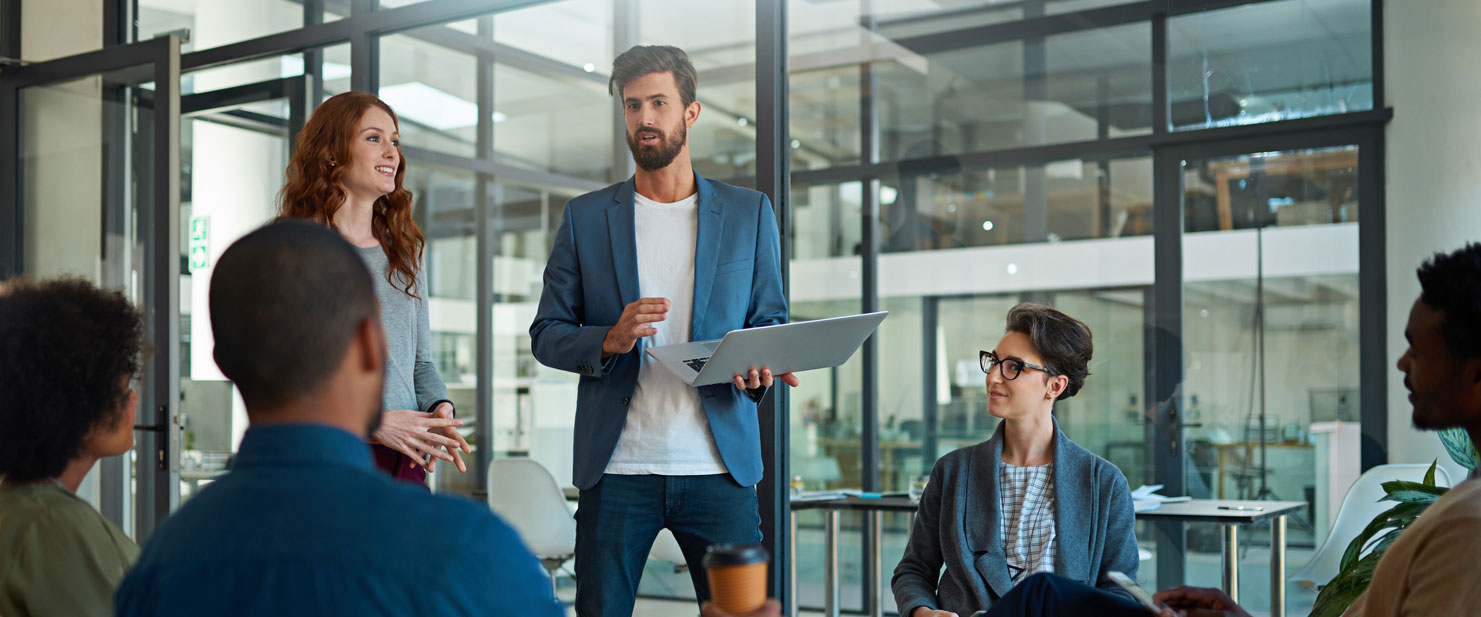 A group of people, including a person and a person, are standing in an indoor space having a conversation about sustainability and business while looking out the window.