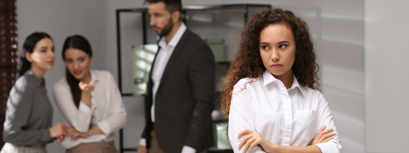 a woman looks annoyed as three coworkers point and gossip about her in the background