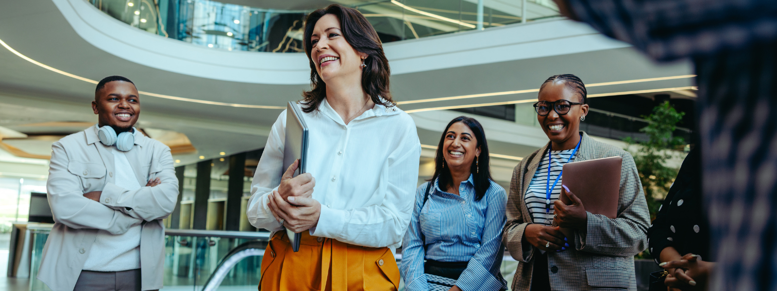 Diverse group of professionals smiling and interacting in a modern office building, conveying a warm, welcoming team environment.