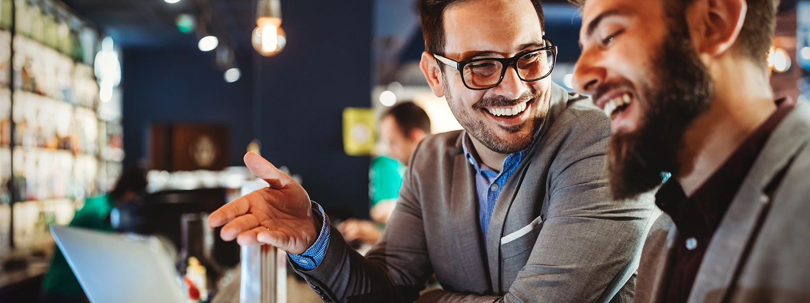 a photo of two businessmen laughing over coffee while looking at a laptop