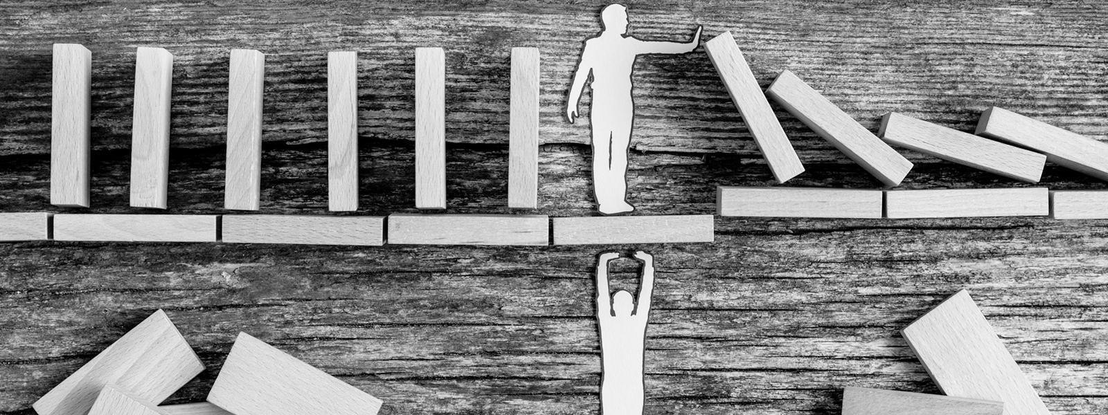 a photo of a person stopping dominoes falling while another person supports the first person from below