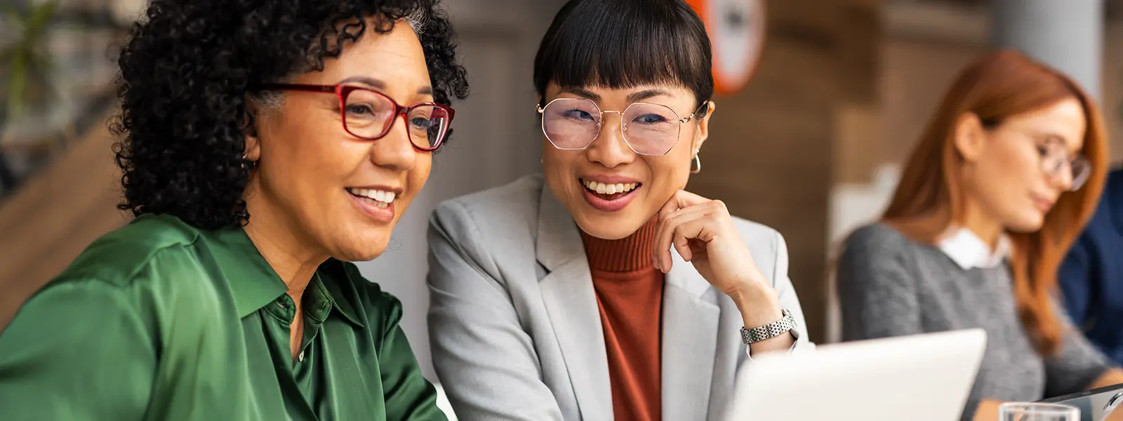A photo of two businesswomen smiling while looking at a laptop